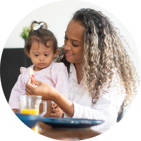 image of a Mother smiling with young daughter on lap, encouraging her to eat.