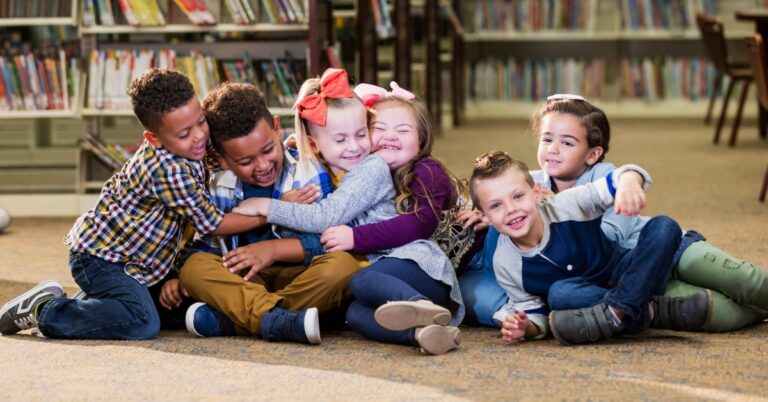group of six young, school aged children playing and hugging on the carpet in a school library.