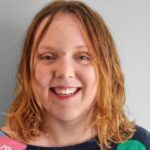 Young person with should length fair hair and red lipgloss, smiling into the camera.