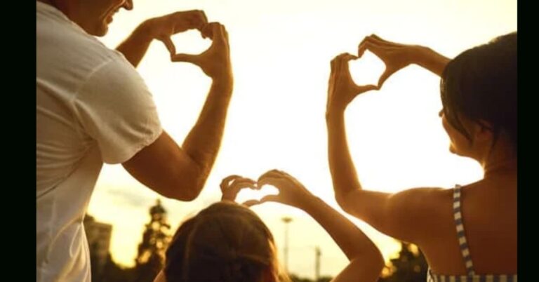 Dad, child and Mum photographed from behind in a sunset holding up their hands in the shape of a heart.