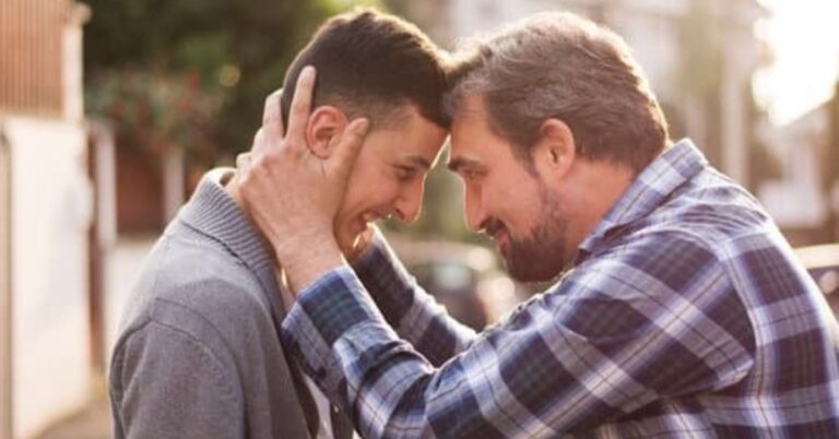 fatherr and son showing affection. The Dad is holding his son's head and pulling him close and smiling into each other.