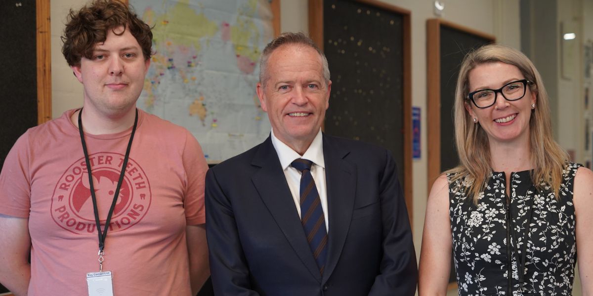 Three people smiling standing next to each other, the person in the middle wearing a suit and tie.