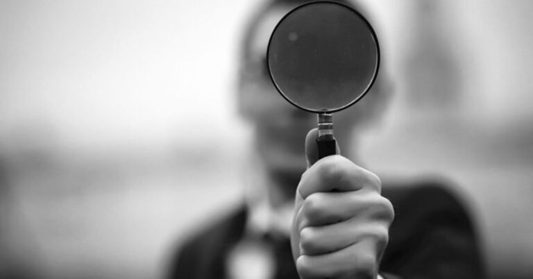 person holding a magnifying glass straight at camera, black and white image.