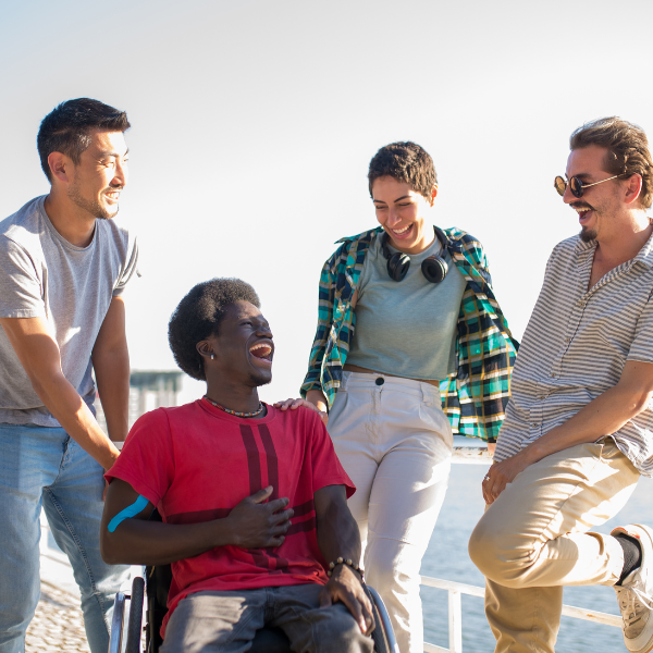 Group of people standing outside looking at each other and smiling. Three people are standing and one is sitting in a wheelchair.