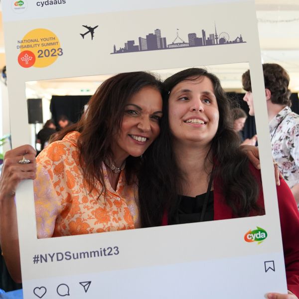 Minister Anne Aly and a young person holding a National Youth Disability Summit, 2023 cut out and smiling together.