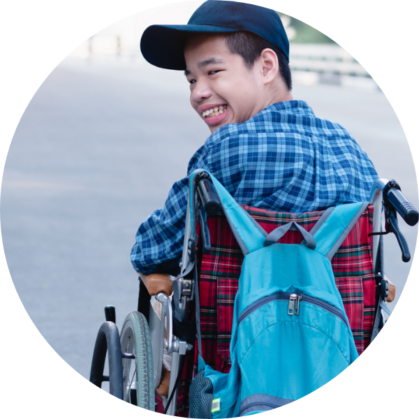 young person in wheelchair looking back and smiling towards the camera. Young person is wearing a navy cap, a navy checked shirt