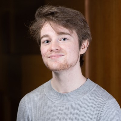 Young person with short light brown hair, smiling into the camera.