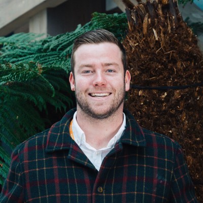 Young person smiling into the camera and standing in front of a tree.