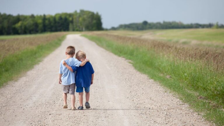 Two young boys on a gravel path, holding each others' shoulders.