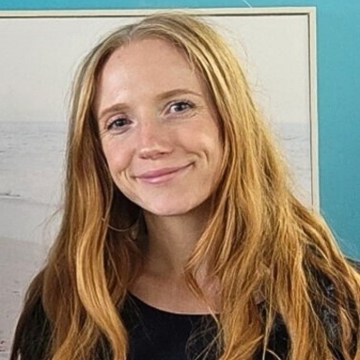 A woman with long, straight strawberry blond hair, freckles, fair skin and a big smile, looking at the camera. She is wearing a black top.