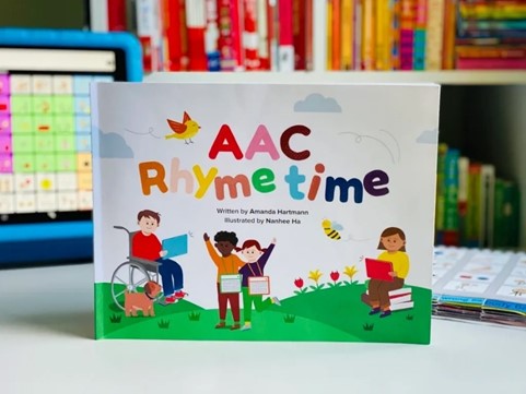 Closeup of the children's book AAC Rhymetime, with an AAC device in the background.