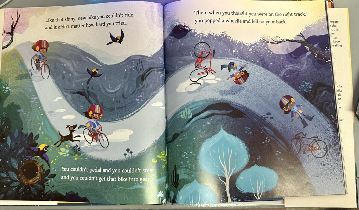 An open page of The Magical Yet featuring an illustration of a girl in a helmet riding a red bike, falling off the bike as rides down a winding, wooded road, observed by a bird flying from its nest and an excited dog. Text reads: Like that shiny new bike you couldn't ride, and it didn't matter how hard you tried. You couldn't pedal, you couldn't steer, and you couldn't get that bike into gear. Then, when you thought you were on the right track, you popped a wheelie and fell on your back."