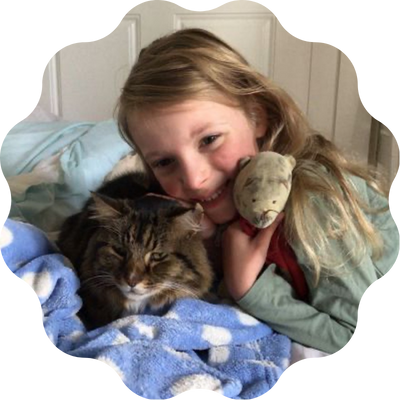 A young girl with long blond hair snuggled up in blankets with a tabby cat.