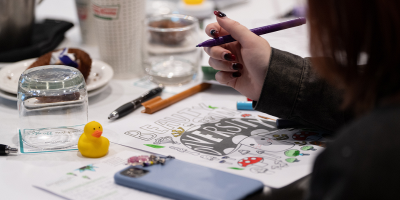 An artist at summit colouring a picture that says "Beauty in Diversity"