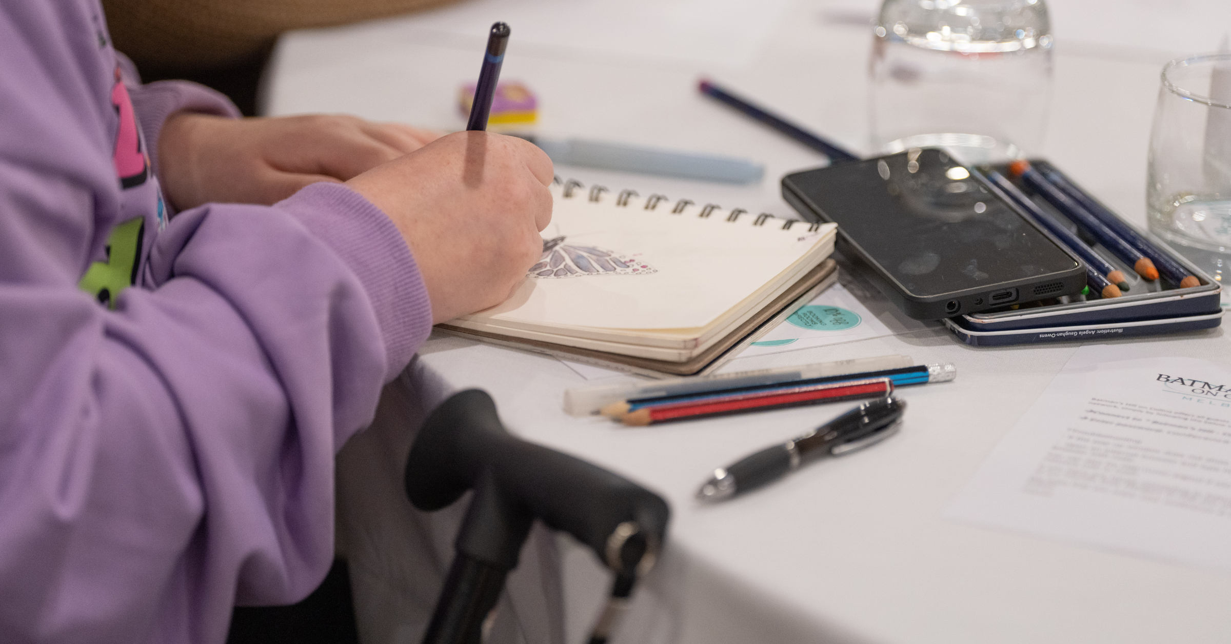 An Artist at summit drawing a butterfly with a pencil. Their walking can is in the foreground.