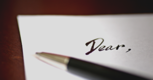 A piece of paper and a pen writing a letter starting with the word 'dear'