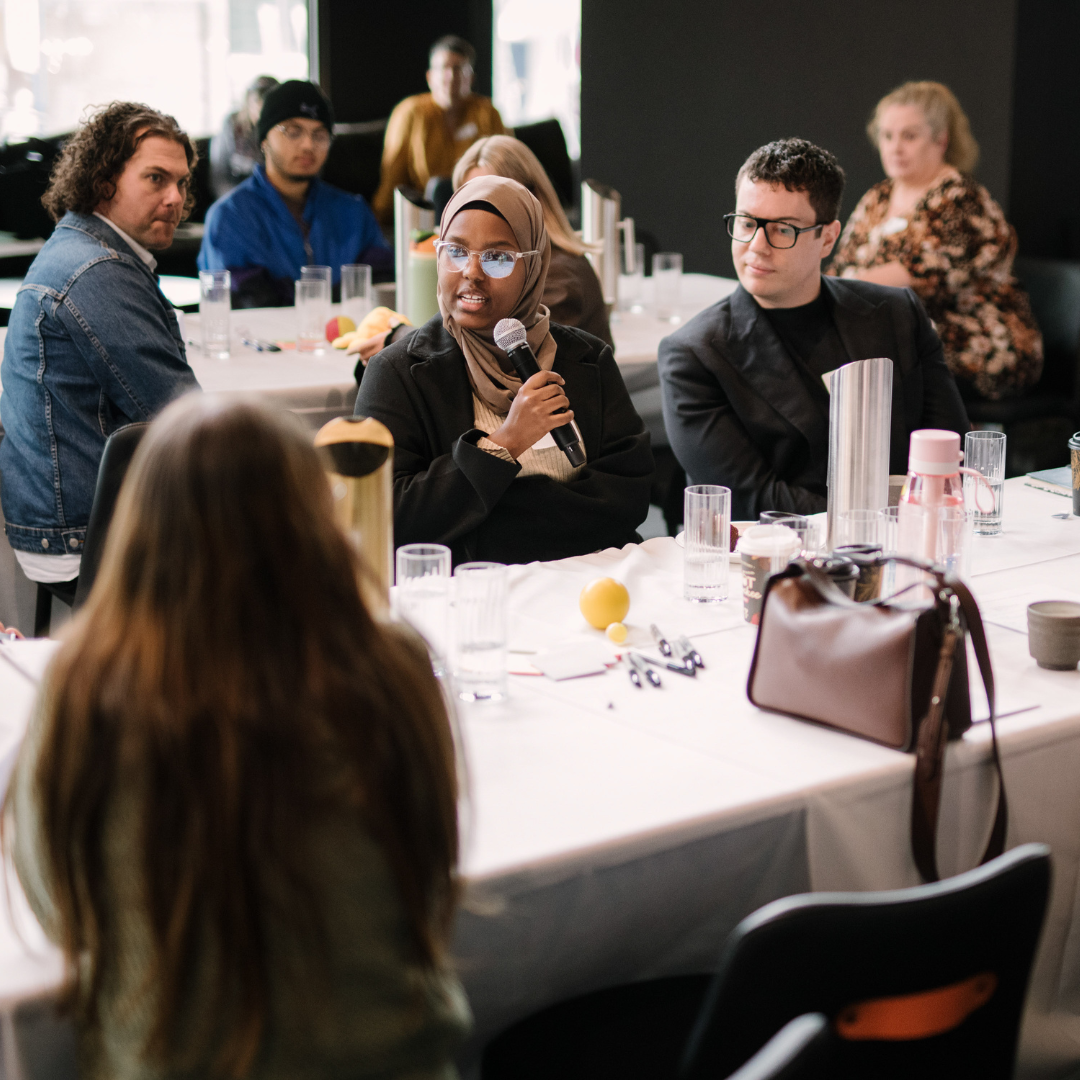 A young woman wearing a hijab speaks to a group of people at the innovation lab