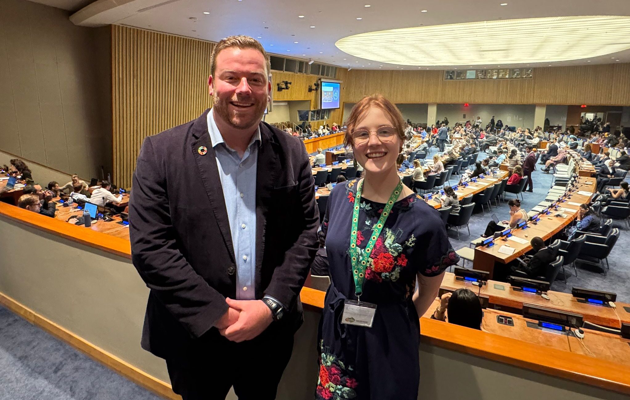 CYDA delegates Jason and Ebe stand together smiling, they are standing on a balcony that overlooks the general assembly.