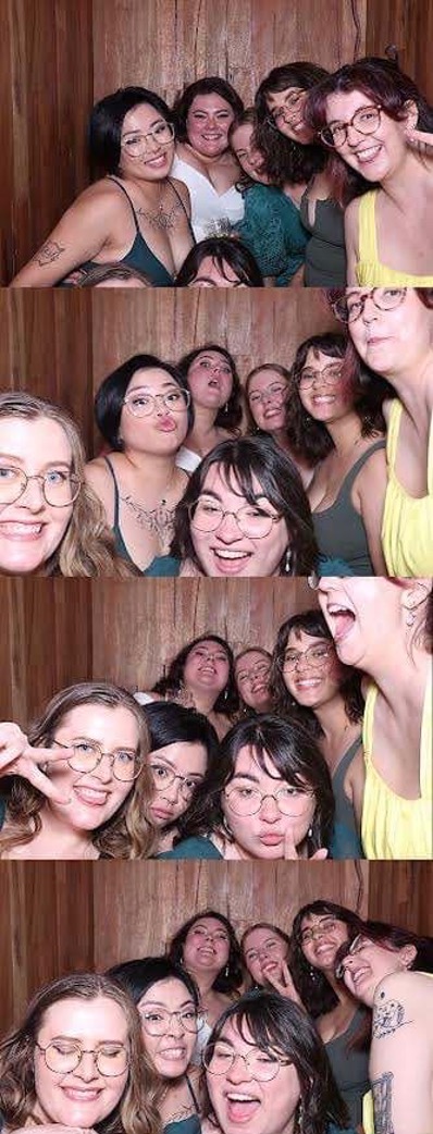 Strip of four photos of seven young women posing together in a photobooth. They are casually dressed in summer clothes. Two have visible tattoos, five are wearing wire-rimmed glassed. In different photos they are smiling, laughing, making kissy faces and making peace signs for the camera.