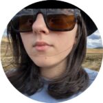 A photo of Faith, a caucasian young woman with long brown hair wearing sunglasses and a blue top.